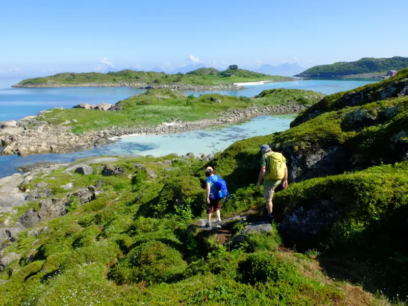 Zwei Wanderer auf einem Küstenpfad mit Blick auf das Meer und die Inseln.