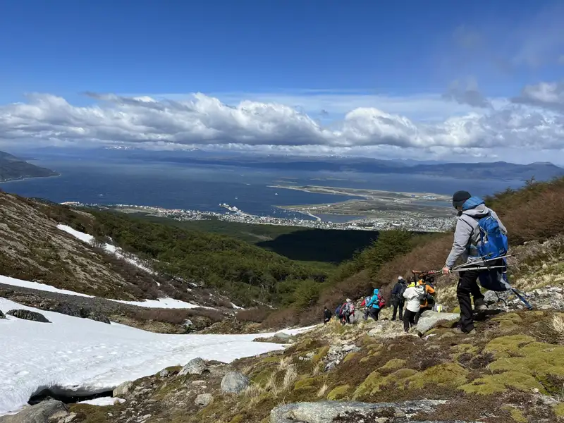 Wandergruppe auf einem Bergpfad mit Blick auf die Küste. Schnee liegt noch am Wegrand.