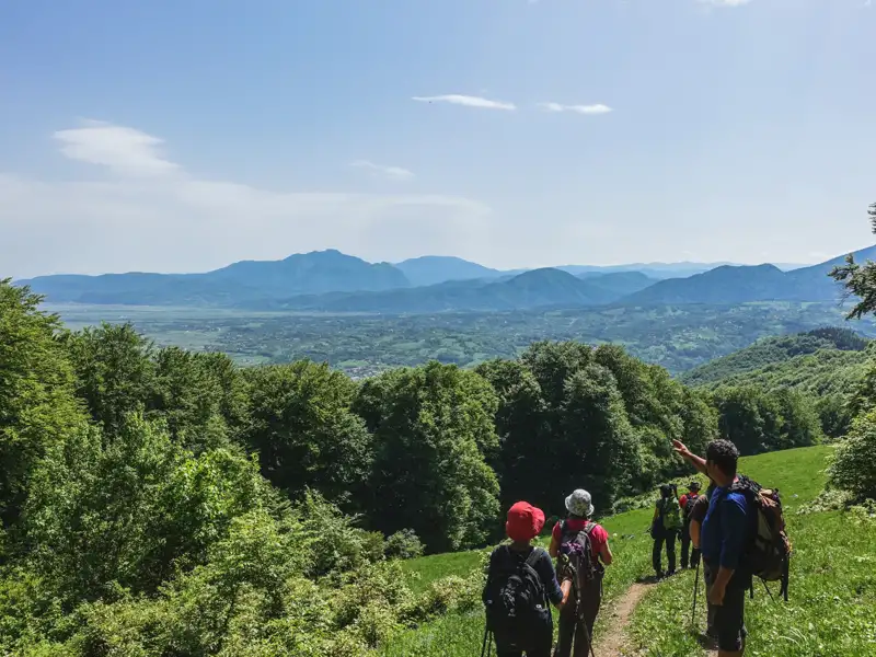Wandergruppe auf einem Bergpfad mit Blick auf eine weite Berglandschaft.