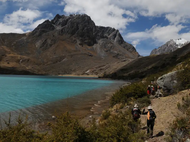 Wanderer auf einem Pfad neben einem türkisfarbenen See in den Bergen.