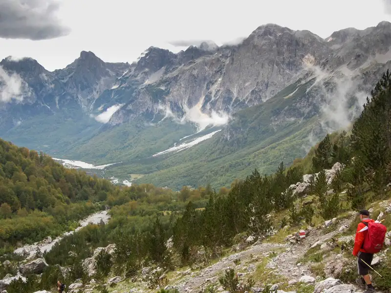 Wanderer auf einem Bergpfad mit Blick auf ein Tal und die umliegenden Berge.