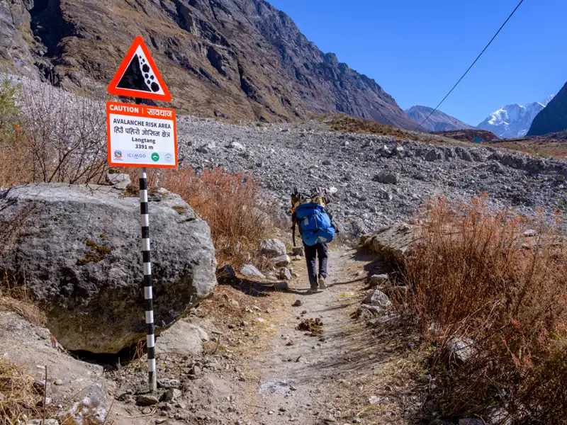 Wanderer in Lawinenrisikogebiet im Himalaya. Ein Warnschild zeigt die Gefahr an.