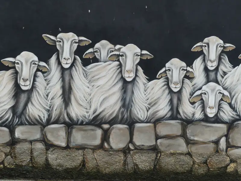 Wandmalerei mit mehreren Schafen hinter einer Steinmauer.
