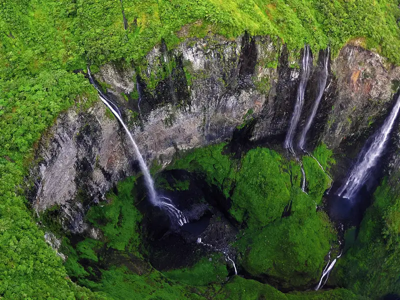 Luftaufnahme eines Wasserfalls, der von steilen Klippen in ein tiefes, grünes Tal stürzt.