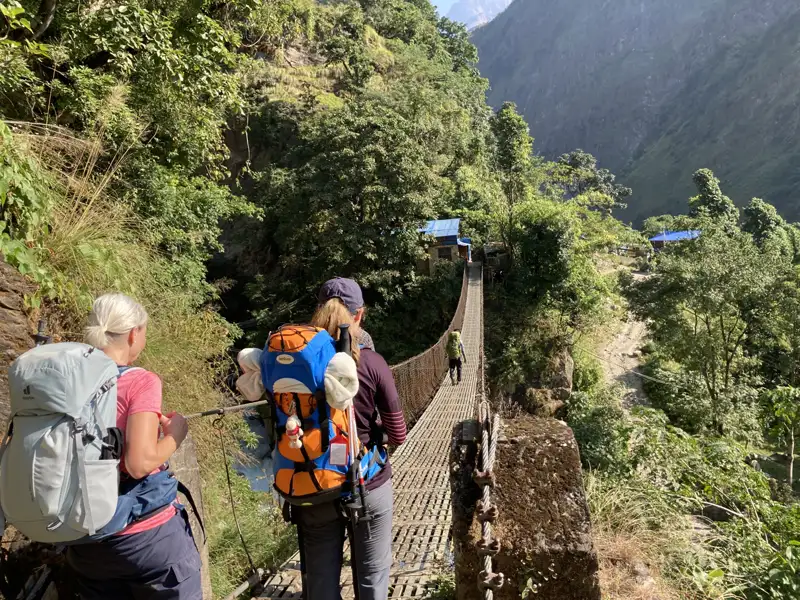 Zwei Wanderer mit Rucksäcken überqueren eine Hängebrücke im Gebirge.