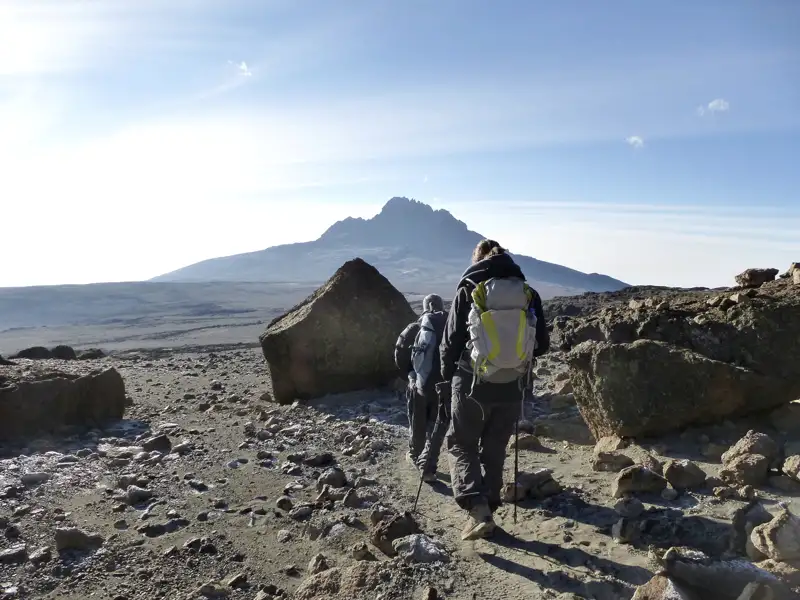 Zwei Wanderer auf einer Bergtour, die felsiges Terrain durchqueren und auf den Gipfel zusteuern.