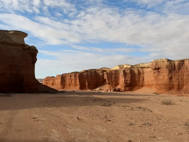 Rote Felsformationen und sandiger Boden unter einem bewölkten Himmel.