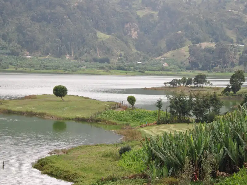 Panoramablick auf einen See mit Inseln, Bäumen und landwirtschaftlich genutzten Flächen, umgeben von Hügeln.