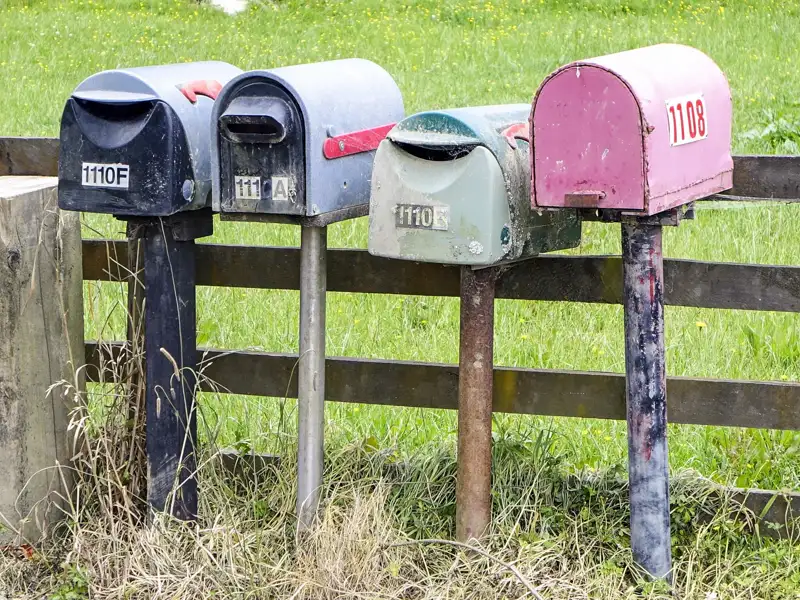Vier Briefkästen mit den Nummern 1110F, 111A, 1110E und 1108 an einem Holzzaun.