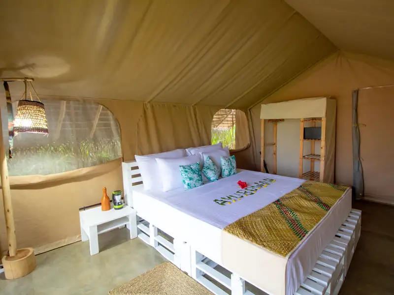 Innenansicht eines Safari-Zeltes mit Bett, Nachttischen und einem Regal.