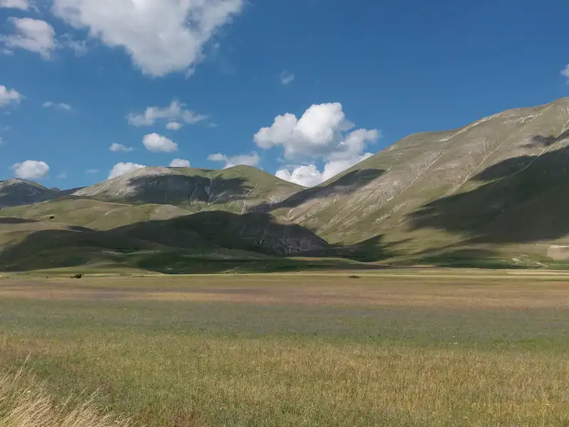Panoramablick auf ein grünes Tal mit Bergen im Hintergrund.