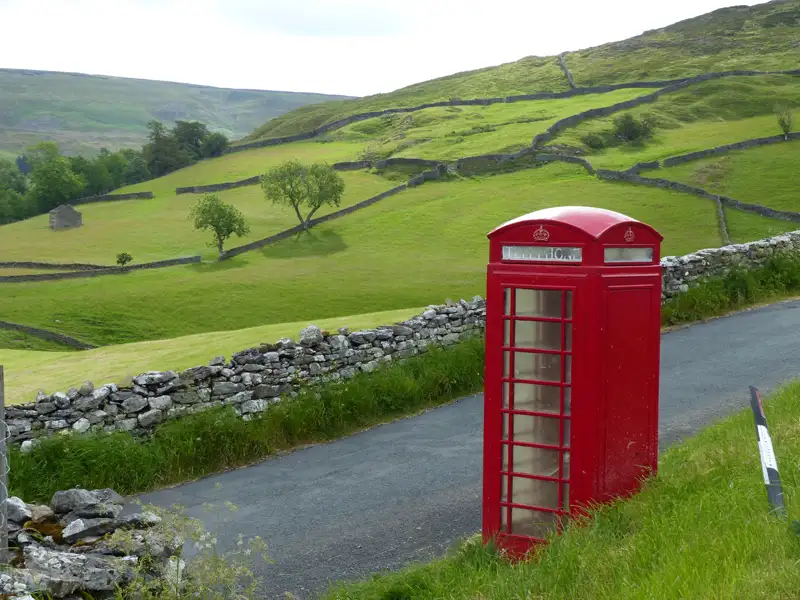Eine klassische rote britische Telefonzelle an einer Landstraße in einer hügeligen Landschaft.