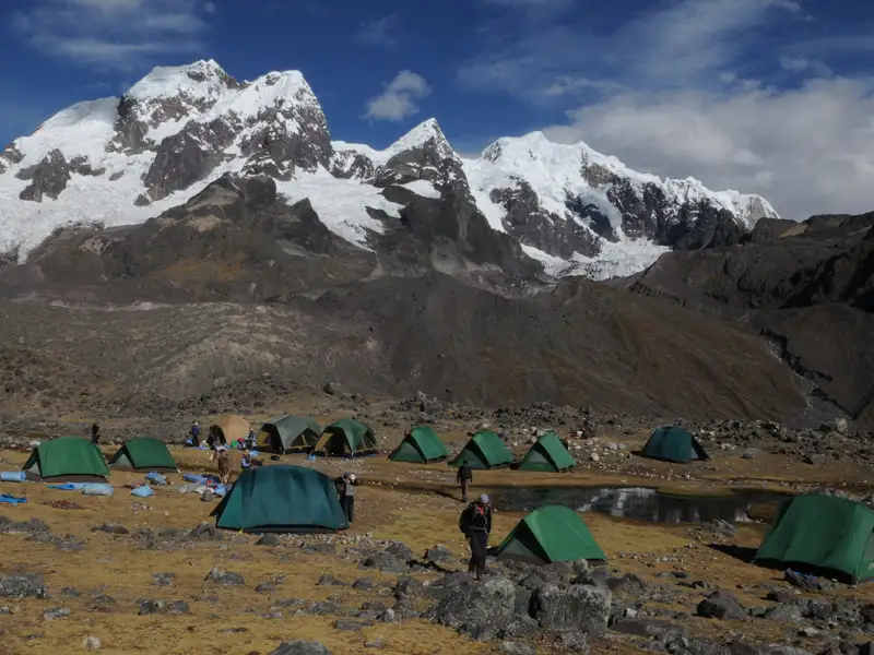 Basislager mit Zelten in einer hochgelegenen Berglandschaft. Schneebedeckte Gipfel und Gletscher im Hintergrund.