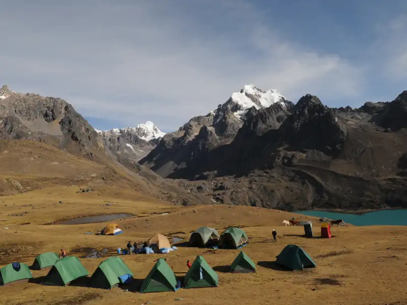 Campingplatz in den Bergen mit Blick auf einen See und schneebedeckte Gipfel.