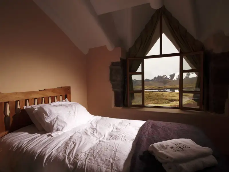 Blick aus dem Schlafzimmerfenster auf eine Berglandschaft mit See.
