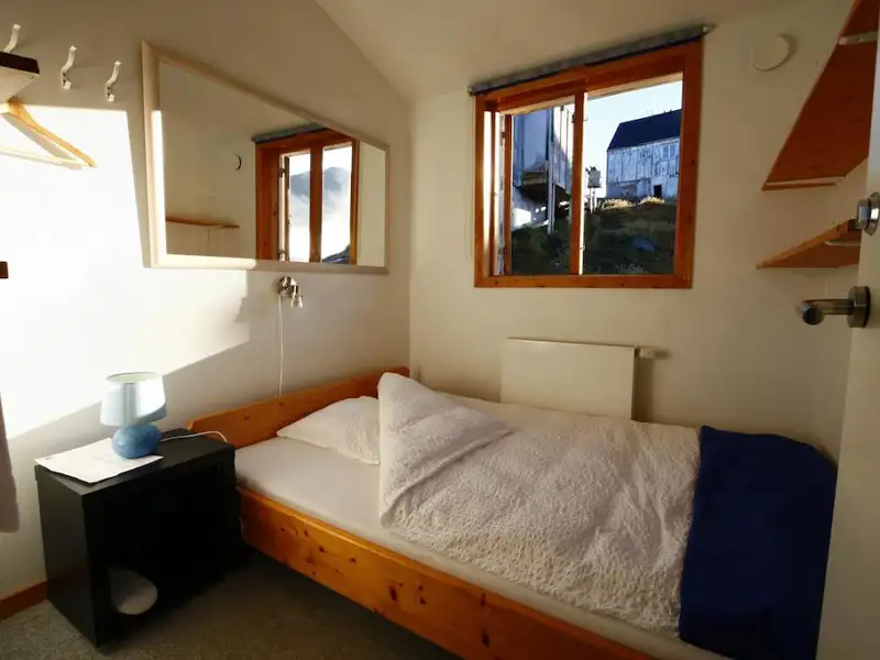 Einzelzimmer mit Bett, Nachttisch und Blick aus dem Fenster auf ein anderes Gebäude.