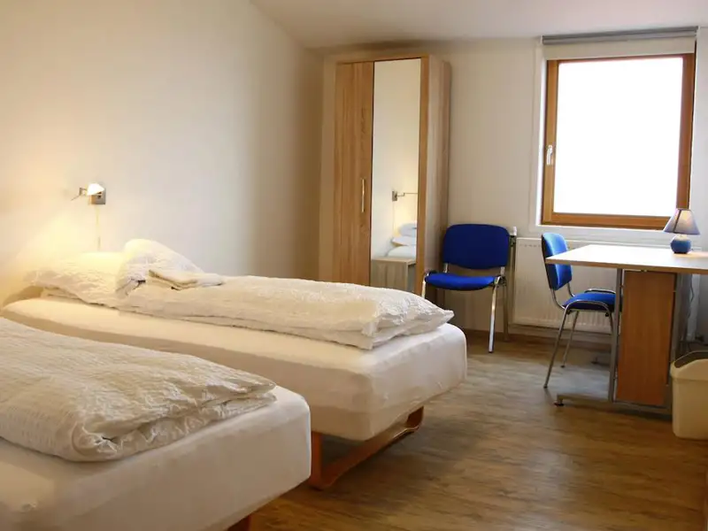 Zimmer mit zwei Einzelbetten, Kleiderschrank und Schreibtisch - ideal für Reisende.