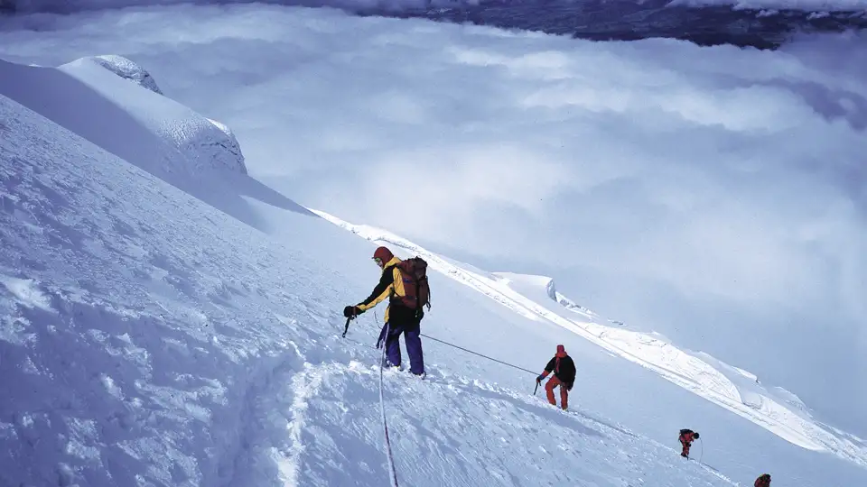 Bergsteiger beim Aufstieg eines verschneiten Berges, gesichert durch ein Seil.