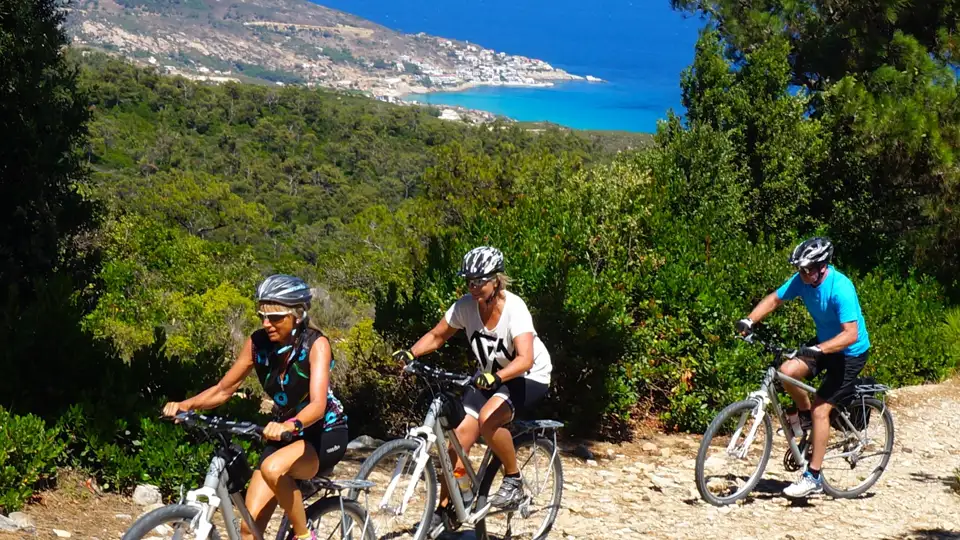 Drei Radfahrer genießen eine Radtour auf einem Küstenweg mit Blick auf das Meer und die Hügel.