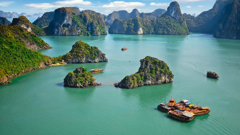 Panorama der Halong-Bucht mit bewaldeten Kalksteininseln und mehreren traditionellen Dschunken.