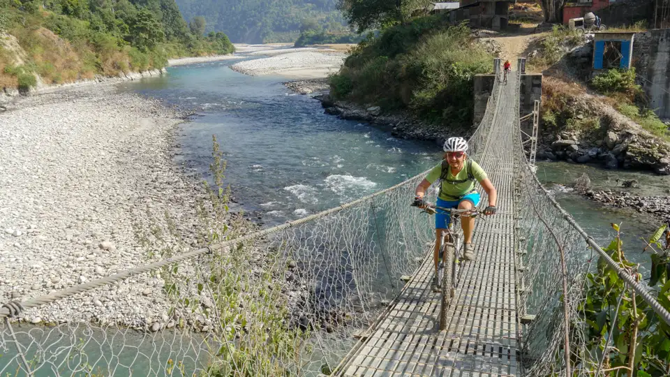 Radfahrer auf einer Hängebrücke über einen Fluss.