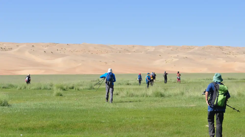 Wandergruppe in einer grünen Oase vor dem Hintergrund von Sanddünen.